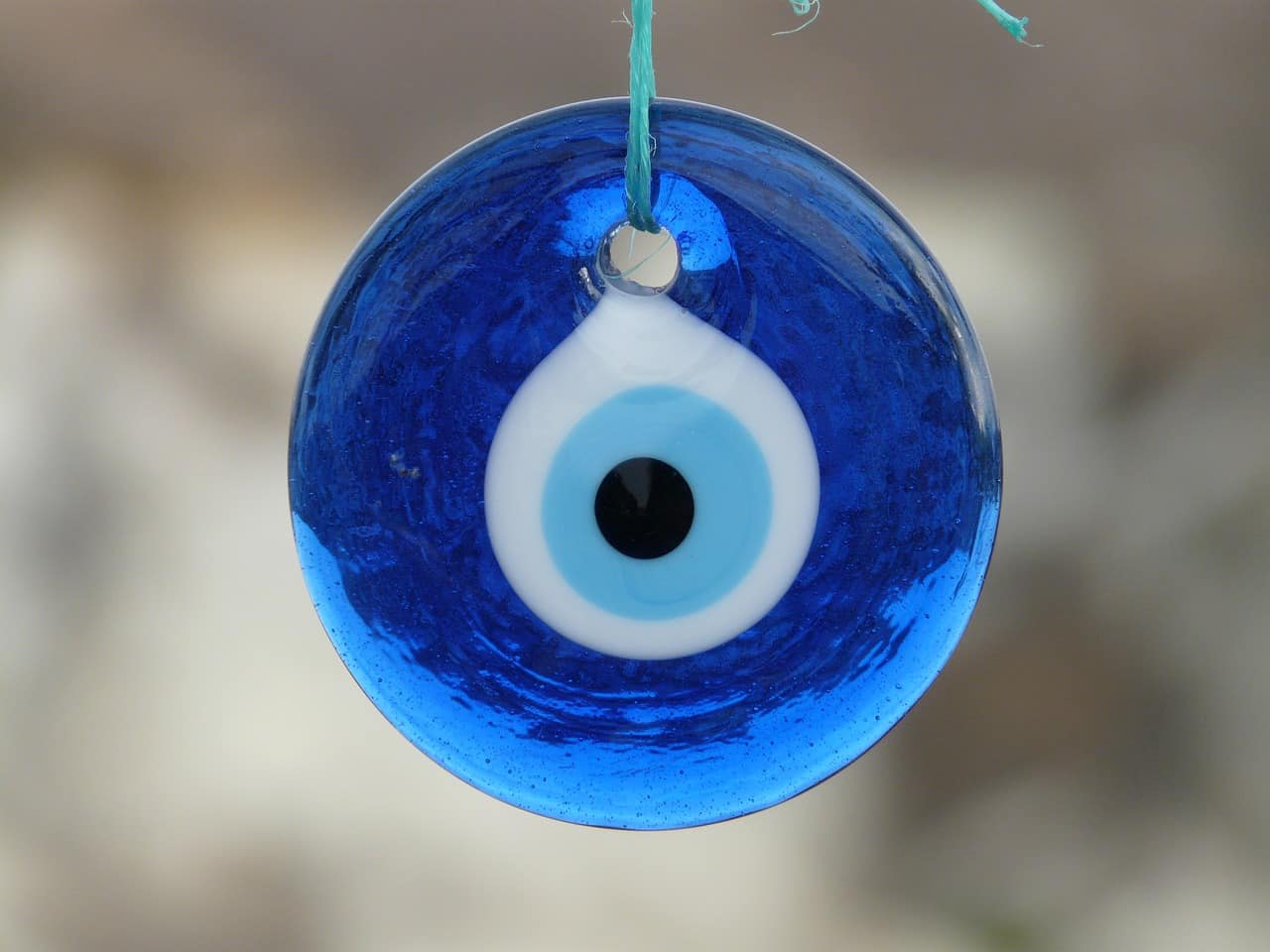Amulette du Nazar boncuk, représentant une sorte d’œil noir, bleu ciel et blanc sur un fond bleu foncé.