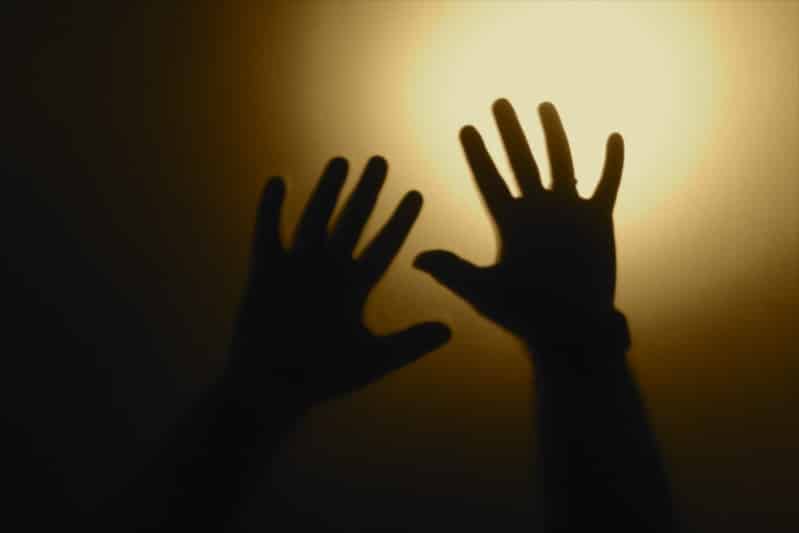 Deux mains en silhouette se détache sur un fond sombre. Une source de lumière se trouve en haut à droite de l’image.