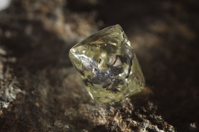 Diamant verdâtre posé sur une surface rocheuse sombre