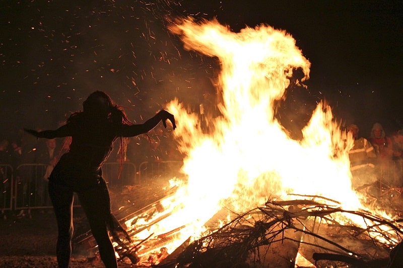 Une femme danse devant un immense feu de joie.