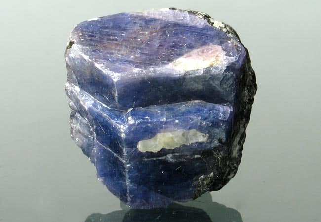 Morceau de saphir brut, à couleur dominante bleu mais avec des zones blanches ou violettes.