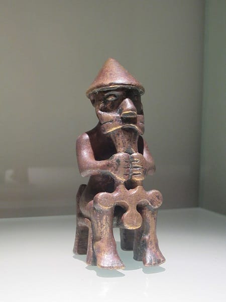 Statuette en bronze représentant une homme casqué sur un trône et tenant devant lui une sorte de marteau ou une croix pointant vers le bas.