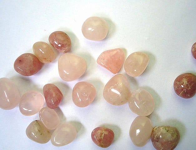 Assortiment de pierres roulées de quartz rose, allant du rose clair au rose foncé, sur fond blanc.