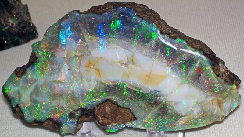 Opale brute blanche au centre et multicolore avec des reflets bleus et verts majoritaires.