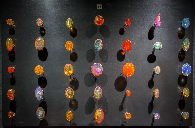 Série d’opales de différentes teintes et tailles exposées sur fond noir sur cinq rangées de sept pierres.